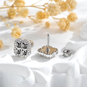 Silver clover stud earrings with black and clear stones on a white artistic display