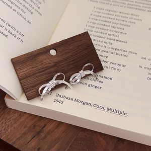 Macro shot of silver bow stud earrings on dark wood display over open book