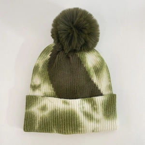 Detail of green and white tie-dye knit beanie with fluffy faux fur pompom and ribbed cuff
