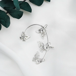 Detailed close-up of silver butterfly ear cuff with textured finish on white silk