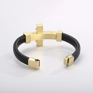 Detail of woven black leather bracelet with golden steel cross and magnetic clasp closure