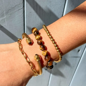 Détail du bracelet en perles œil de tigre et maillons dorés superposés sur le poignet