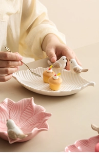 Detail of leaf-shaped ceramic snack plates with bird sculptures in white and pink