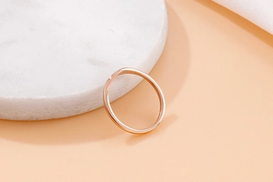 Polished rose gold wave ring with V-shape curve resting on marble tray detail