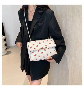 Detail of white envelope crossbody bag with red strawberry prints and gold chain strap