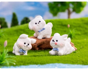 Three cute miniature white resin puppies with blue bows on green moss landscape