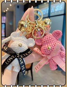 Detail of pink and white resin bears with woven texture and gold keychains held by hand
