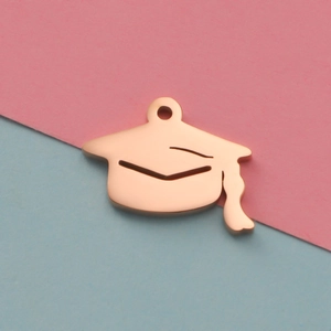 Polished rose gold graduation cap pendant with tassel on pink and blue backdrop