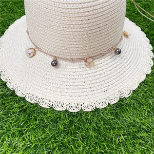 Détail d'un chapeau de paille à bord ondulé avec des perles noires sur herbe verte