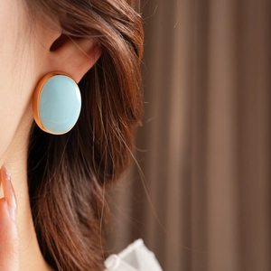 Close-up of a model wearing light blue oval enamel earrings with gold metal edges