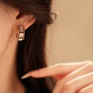 Close-up of C-shaped gold plated earrings with brown enamel and square zircons on model