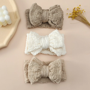Flat lay of three oversized baby bow headbands in white, beige, and light brown colors