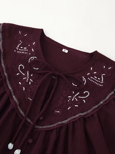 Close-up of bohemian embroidered neckline with white beads and tie-up bow on burgundy top