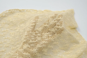 Close-up of soft pale yellow crochet lace fabric showing transparency and delicate texture