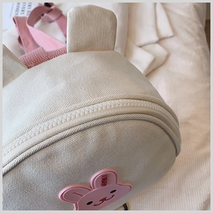 Close-up of canvas texture and zipper detail with a pink rabbit badge on a beige backpack