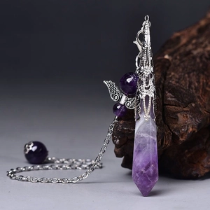 Macro shot of natural amethyst hexagonal crystal pendant with silver wing charms on wood