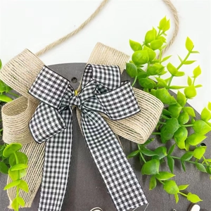 Detail of wooden welcome sign with buffalo plaid bow, burlap, and faux green leaves