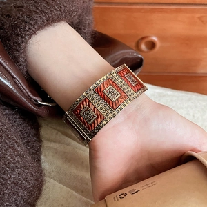 Detail of vintage gold-toned cuff bracelet with red spiral enamel patterns on wrist