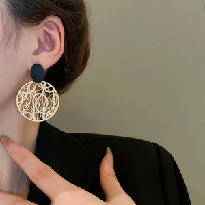 Detail von goldenen Hohlnetz-Ohrringen mit schwarzen Steckern am Modell für Eleganz