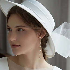 Elegant gold long tassel pearl earrings on model wearing a white wide-brimmed hat