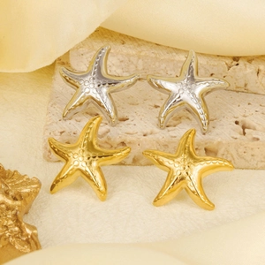 Macro shot of 18k gold and silver starfish earrings on a textured stone surface