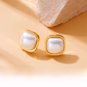 Macro detail of square gold-plated earrings with inset white pearl on a stone base