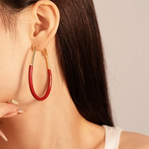 Close-up of model wearing large red enamel and gold teardrop hoop earrings for women