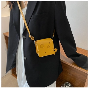 Close-up of a small yellow cheese-shaped crossbody bag featuring unique hole details