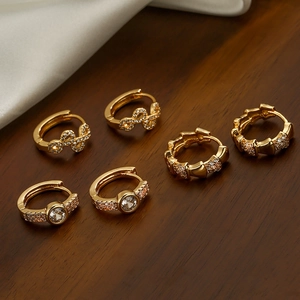 Three pairs of gold-plated copper hoop earrings with sparkling zircon on silk background
