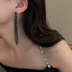 Side profile of a model wearing long black fringe earrings with geometric rhinestone details