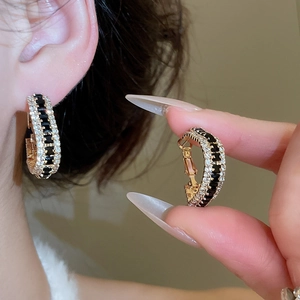 Detail of wide U-shaped gold earrings featuring black rectangular and white pavé zircons