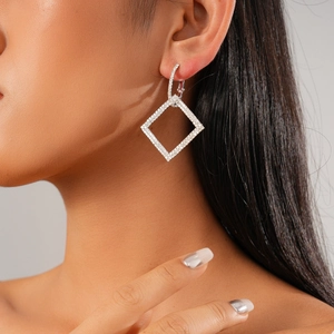 Macro shot of silver geometric diamond earrings worn by a model in soft studio lighting