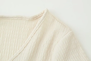 Macro view of textured crepe fabric and refined V-neckline stitching on beige top