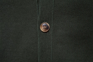Detail of dark green knit fabric with a premium marble-textured brown button