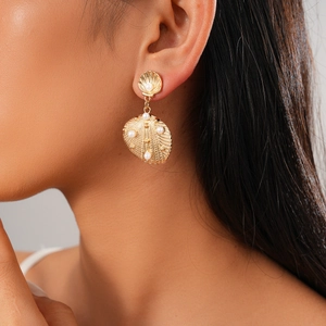 Close-up of gold shell earrings with pearls on model's ear for beach vacation style