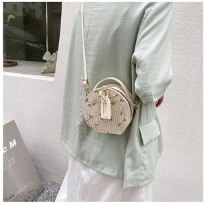 Model wearing round woven straw crossbody bag with floral embroidery and PU strap