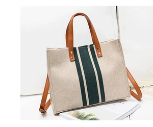 Close-up of canvas tote bag with green stripes, brown leather handles and shoulder strap