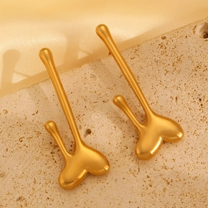 Macro view of polished gold teardrop earrings on textured stone with silk fabric