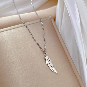 Vue macro d'un collier pendentif plume argentée sur fond de tissu en soie blanche
