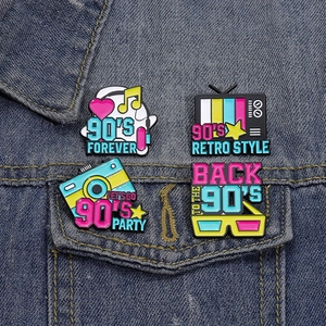 Close-up of retro 90s enamel pins featuring TV and camera on denim jacket