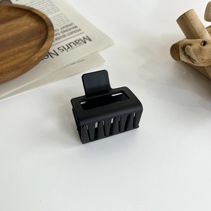 Detail shot of a black matte square hair claw clip on a wooden display tray