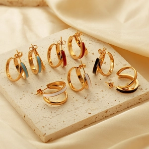Detail view of gold C-shaped earrings with colorful enamel on textured marble and silk