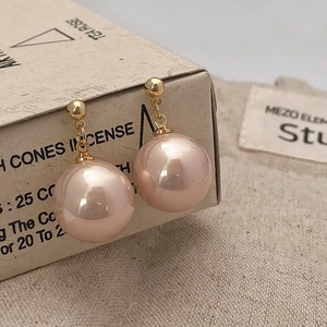 Detailed macro view of pink pearl drop earrings with golden metal studs on a rustic box