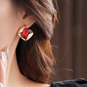 Close-up of gold earring set with a rectangular red gemstone on a model's ear
