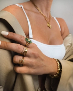 Detail shot of a gold snake ring with green zircon stones worn with layered jewelry