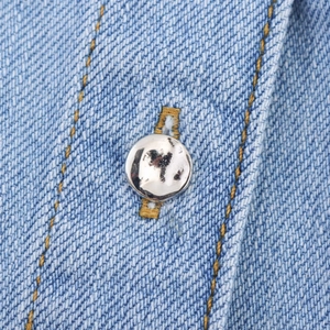Detailopname van lichtblauwe denim stof met zilveren knopen en gele dubbele stiksels
