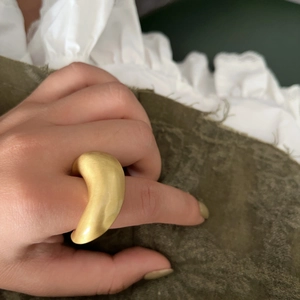 Detailopname van een grote goudkleurige matte ring met een gebogen ontwerp