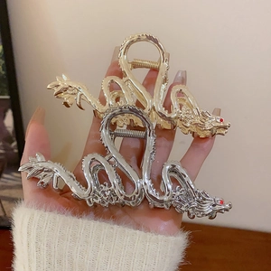 Détail de deux pinces à cheveux en métal doré et argenté aux formes de dragon uniques