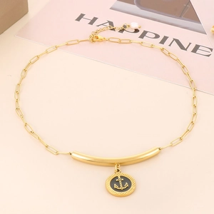 Macro shot of gold paperclip chain necklace with black anchor charm on beige background