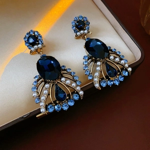 Close-up of vintage gold pearl earrings with blue gemstones on beige satin lining